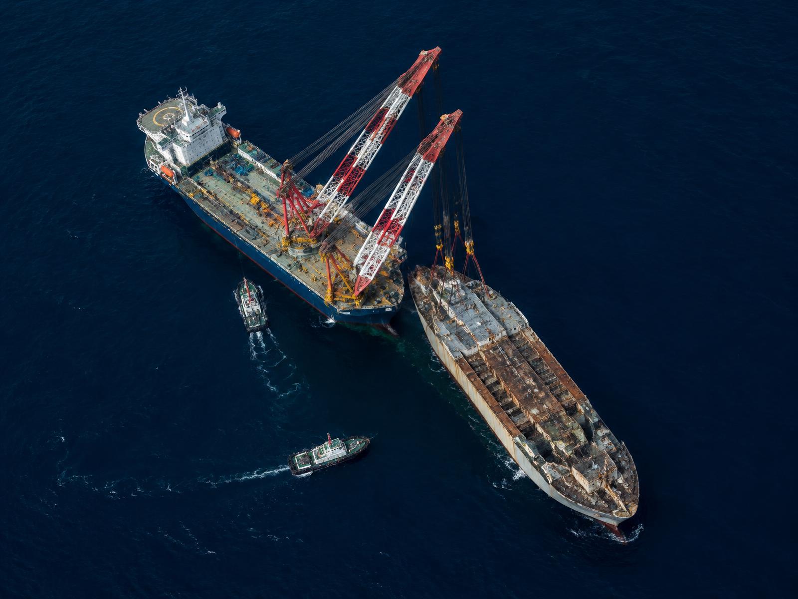 Aerial view of a heavy-lift salvage operation with support tugs